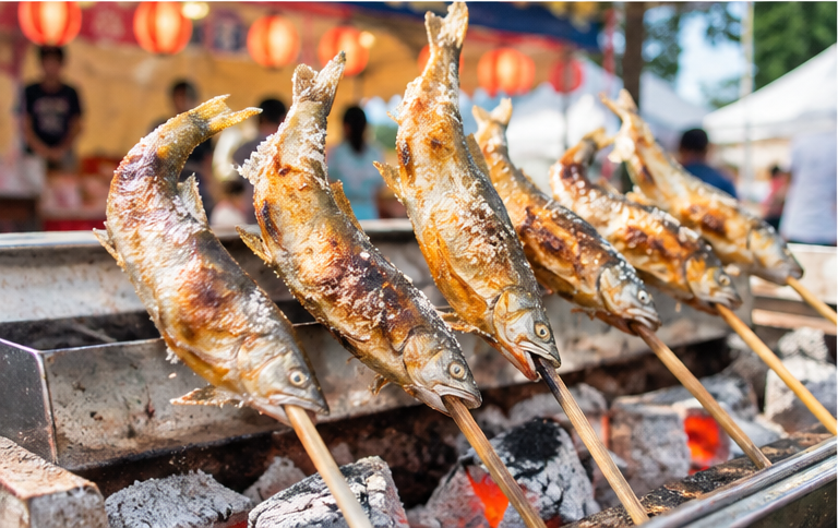 Salt-grilled ayu cooking over charcoal at a Japanese summer event.